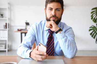 Ofisinde cep telefonu olan yakışıklı genç bir iş adamı.