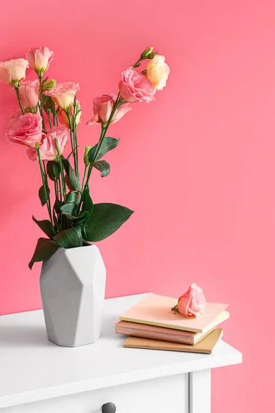 Vase with roses and books on table near pink wall