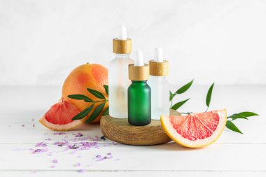 İçinde greyfurt şişeleri bulunan kompozisyon temel yağ ve hafif ahşap masa üzerindeki meyveler