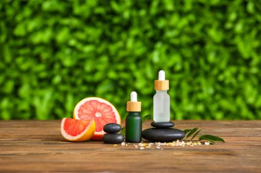 Dışarıdaki ahşap masa üzerinde greyfurt yağı ve spa taşı şişeleri ile kompozisyon