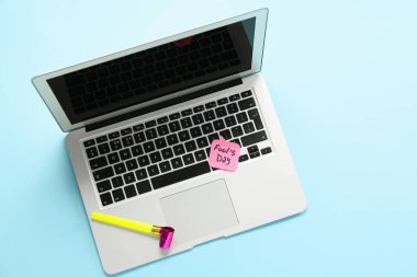 Dizüstü bilgisayar, parti ıslığı ve renkli arkaplanda FOOL 'un Günü yazılı yapışkan not