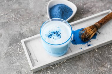 Bir bardak mavi kibrit çayı, gri grunge arka planda pudra ve kase.