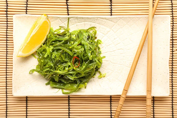 Sağlıklı deniz yosunu salatası, limon ve bambu hasırı üzerinde çubuk, yakın plan.
