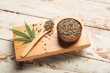 Beyaz ahşap arka planda kenevir tohumları olan kase ve kaşık.