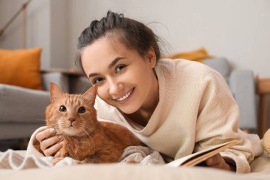 Güz günü evde güzel kızıl kedisi ve kitabı olan bir kadın.