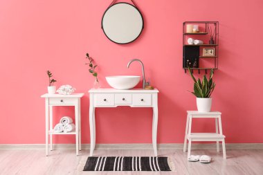 Lavabosu, aynası ve pembe duvarı olan şık bir banyo.