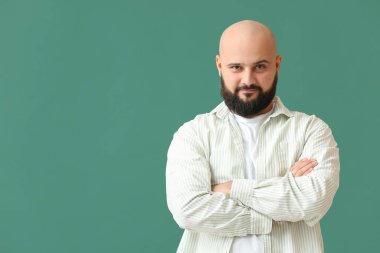 Yeşil arka planda çapraz kollu yakışıklı kel adamın portresi.
