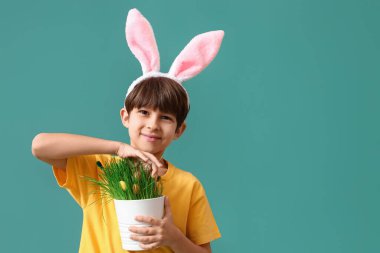 Tavşan kulaklı şirin bir çocuk elinde paskalya yumurtaları ve renk arka planında fırçalarla ev bitkisi tutuyor.