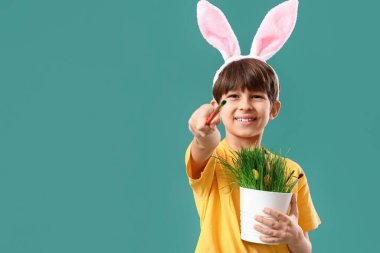 Tavşan kulaklı şirin bir çocuk elinde paskalya yumurtaları ve renk arka planında fırçalarla ev bitkisi tutuyor.