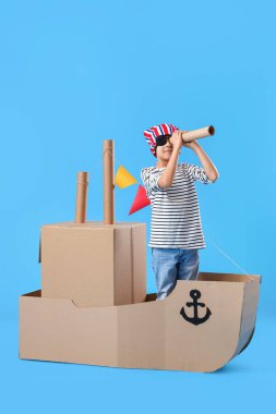 Mavi arka planda karton gemiyle oynayan sevimli küçük çocuk.