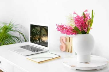 Masada güzel sümbül çiçekleri ve beyaz duvarın yanında modern dizüstü bilgisayar.