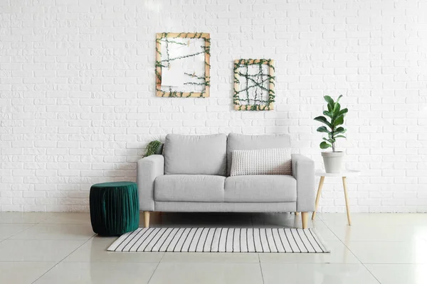 Stylish sofa, pouf and houseplant near white brick wall