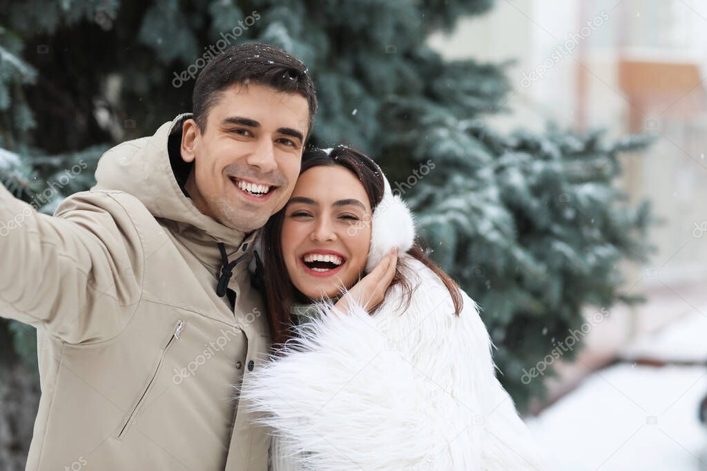 Loving couple taking selfie in park on snowy winter day