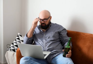 Bilgisayarlı bir adam evde bira içiyor.