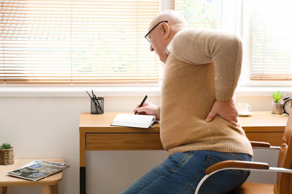 Senior Mit Rückenschmerzen Schreibt Hause Notizbuch — Stockfoto