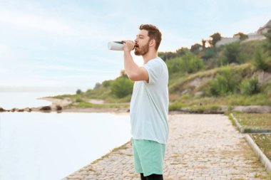 Nehir kenarındaki eğitimden sonra su içen yakışıklı adam.