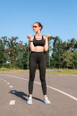 Açık havada esneme bandı olan genç bir kadın.