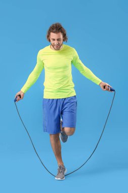 Mavi arka planda ip atlayan sportif bir adam.