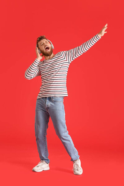 Cool dancing young man listening to music and singing on color background