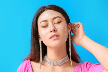 Parlak makyajlı ve mavi arka planda kapalı gözlü Asyalı kadın.