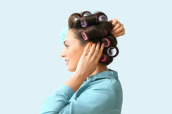 Beautiful young woman in hair rollers on light background