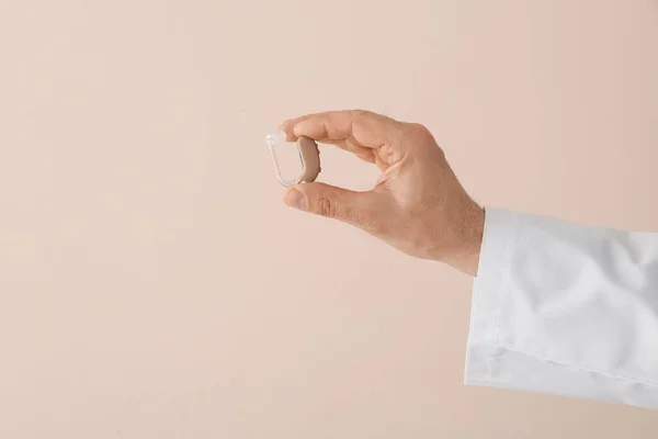 Hand of doctor with hearing aid on light background