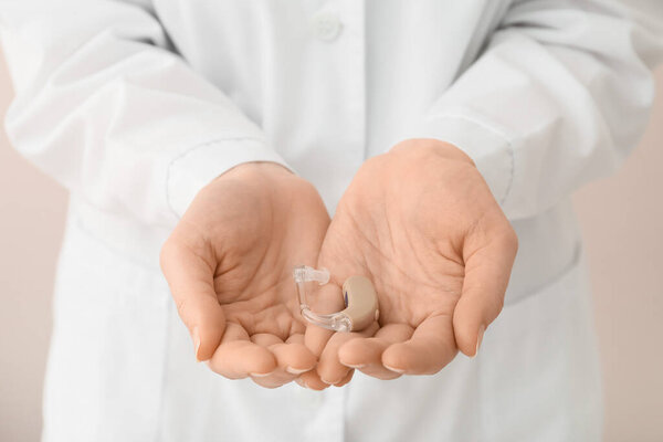 Doctor with hearing aid on light background, closeup