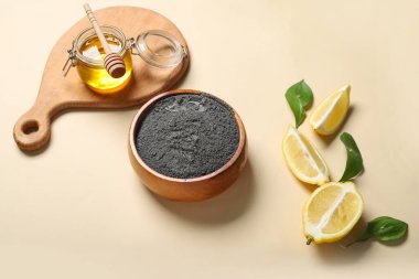 Yüz maskesi için bir kase etkinleştirilmiş karbon tozu, arkaplanda limon ve bal