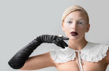 Yaratıcı makyajı ve gri arka planda zarif eldivenleri olan güzel bir genç kadın.