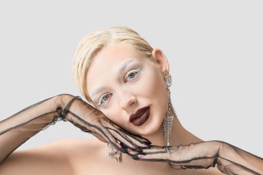 Yaratıcı makyajı ve gri arka planda zarif eldivenleri olan güzel bir genç kadın.