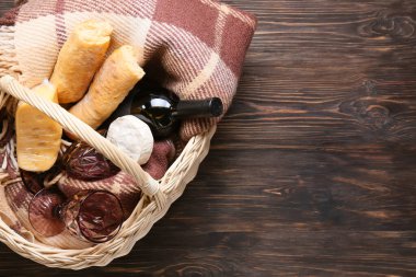 Tahta arka planda piknik için lezzetli yemek, şarap ve ekoseli sepet.
