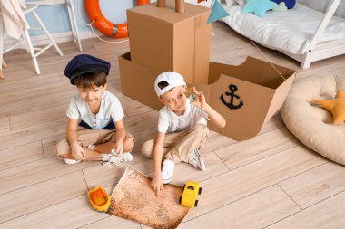 Evde karton gemi ve haritayla oynayan komik küçük çocuklar.