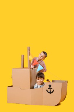 Sarı arka planda karton gemiyle oynayan komik küçük çocuklar.