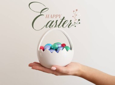 Paskalya tebrik kartı ve kadın eli çikolata yumurtası sepeti.