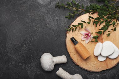 Kozmetik ürünleri, bitki torbaları ve koyu arkaplanda spa taşlarıyla kaplıca kompozisyonu