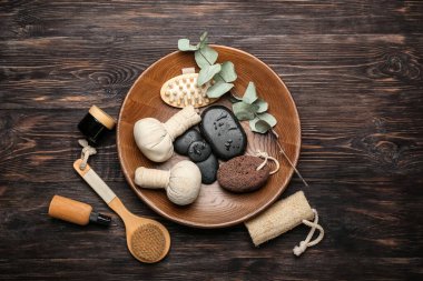 Banyo malzemeleri, spa taşları ve ahşap arka planda bitki torbalarıyla dolu tepsi.