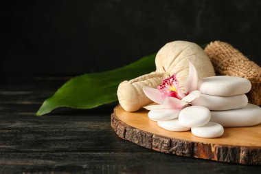 Orkide çiçekli spa taşları ve siyah ahşap arka planda bitki torbası.