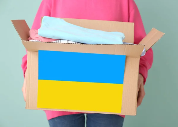 Woman holding box with humanitarian aid for Ukraine on color background