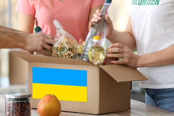 Volunteers putting products in box with Ukrainian flag. Humanitarian aid for Ukraine