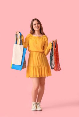 Pembe arka planda çevre çantaları olan güzel genç bir kadın.