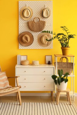 Çekmeceler, sapkalı tahta ve sarı duvarda asılı çanta.