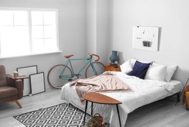 Işık duvarının yanında bisikleti olan şık bir yatak odası.