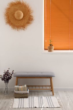 Modern bank, okaliptüslü vazo ve ışık duvarına yakın kitaplar.