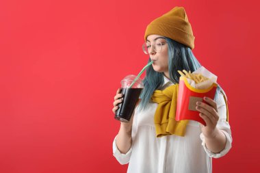 Sıra dışı saçları olan genç bir kadın kola ve patates kızartması tutuyor.