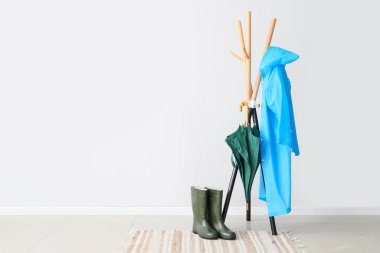 Mavi yağmurluk, şemsiye ve çizmelerle aydınlık duvarın yanında