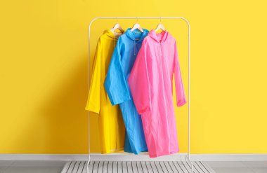 Sarı duvarın yanında renkli yağmurluklarla dizilin.