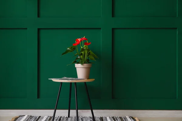 Modern table with Anthurium flower and magazine near green wall