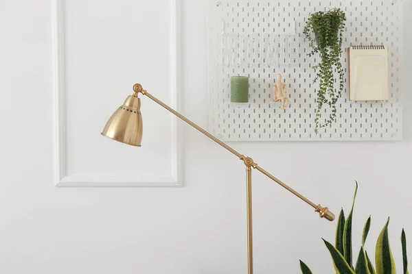 黄金のスタンディングランプ 装飾と観葉植物が光の壁にかかっているペグボード — ストック写真