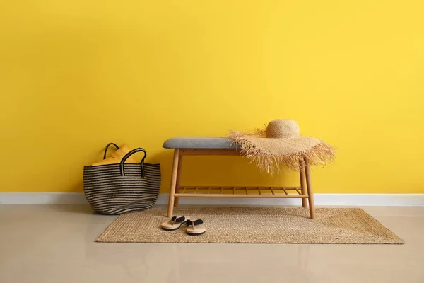 黄色の壁の近くの帽子 フリップフロップ バッグ付きの快適なベンチ — ストック写真