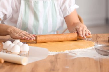 Olgun bir kadın mutfaktaki masada kurabiye için hamur topluyor.
